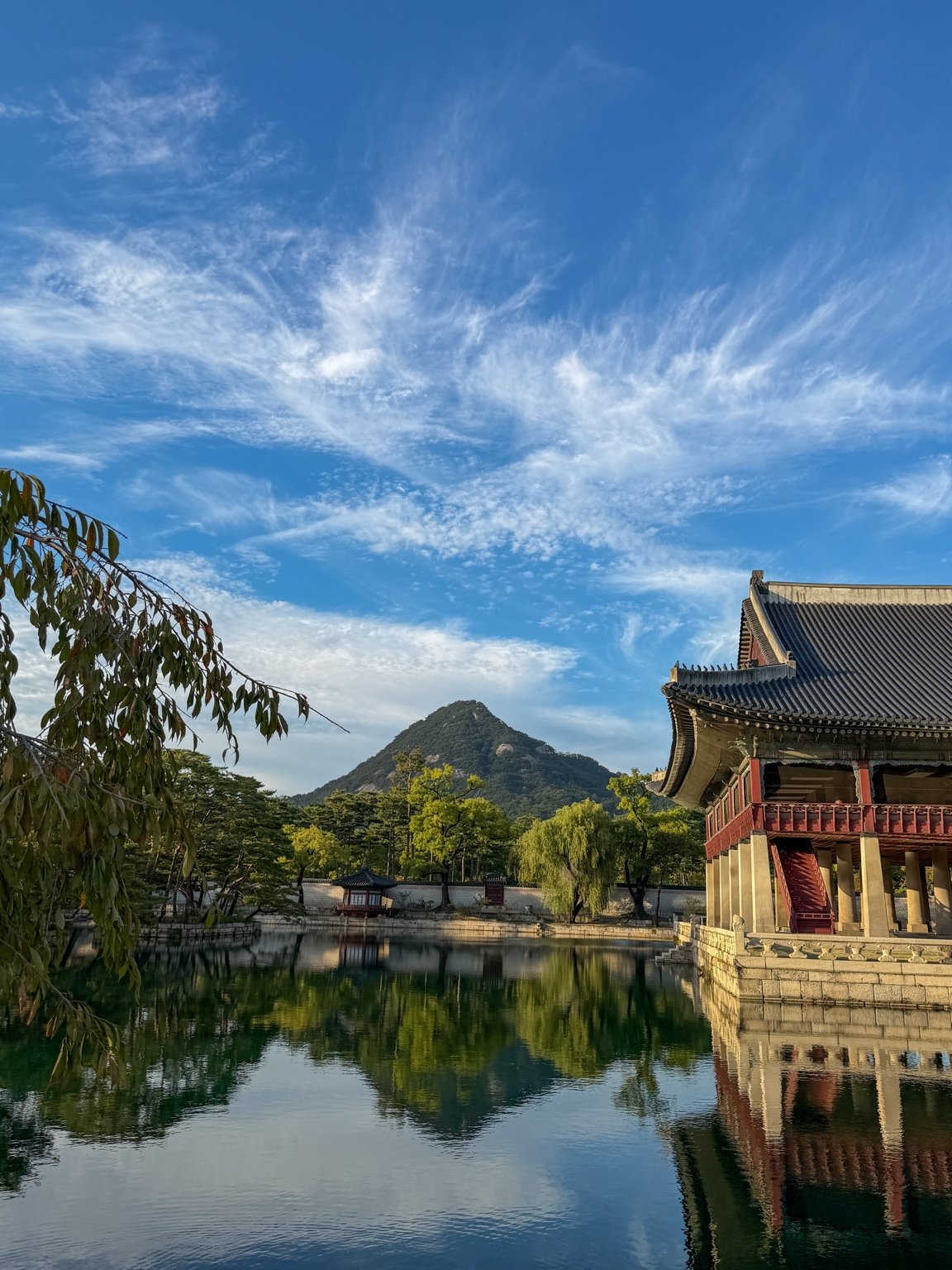 Gyeonghoeru Pavilion beside its reflecting pond, with trees and a mountain beneath a blue sky