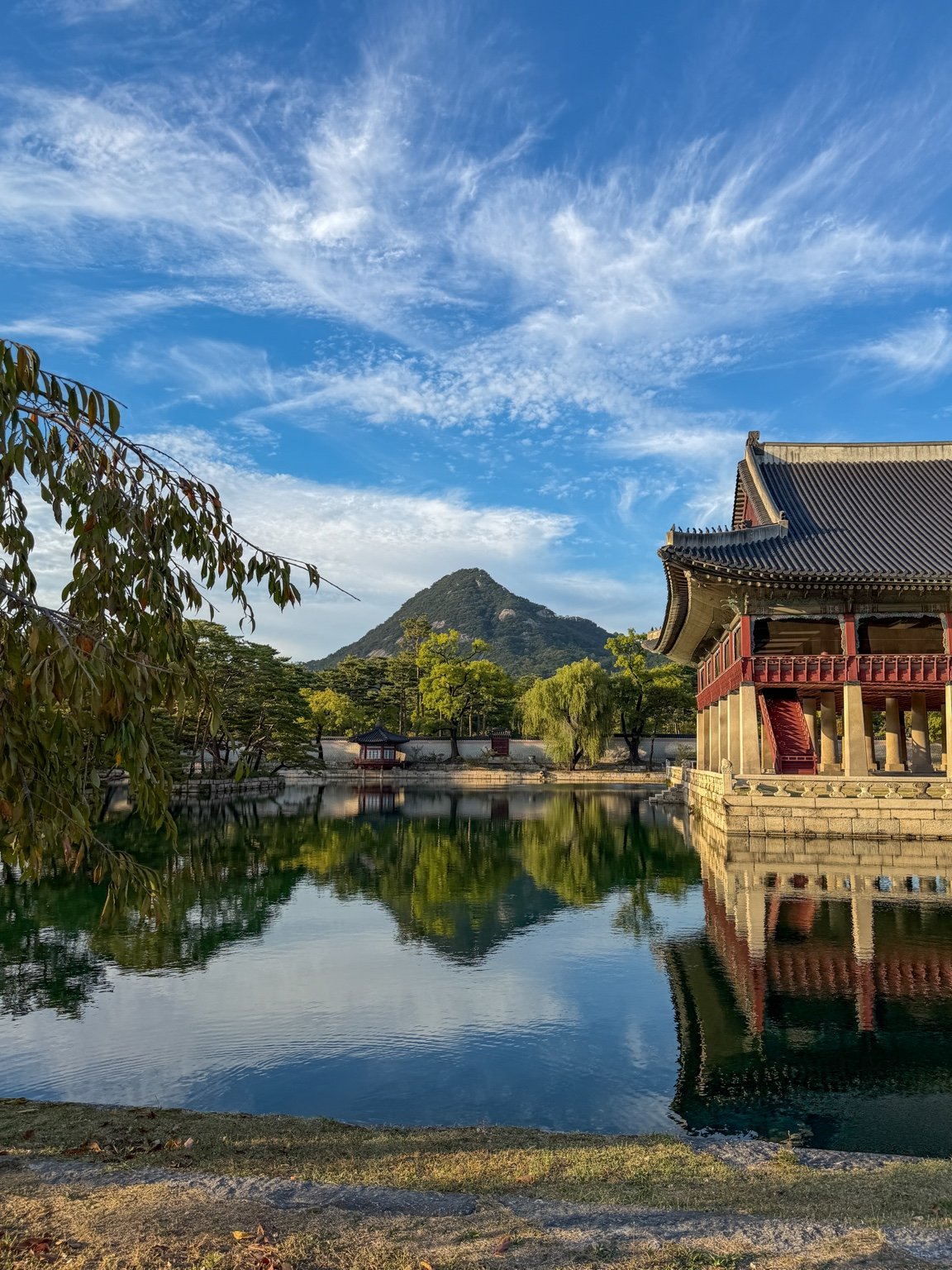 Gyeonghoeru Pavilion reflected in its pond, with the grassy bank in the foreground